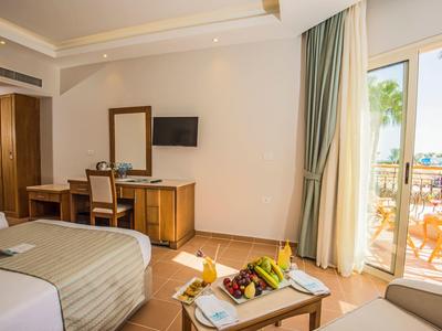 Habitación de hotel luminosa con camas, balcón y vista al mar bajo cielo despejado.