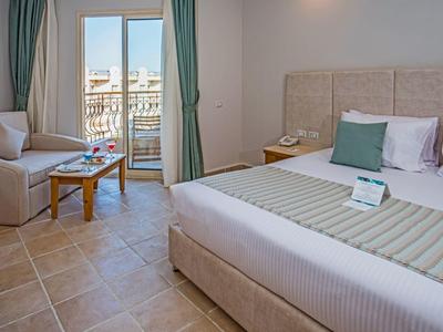 Habitación de hotel con cama grande, sofá, mesa de madera y balcón con vista al exterior.