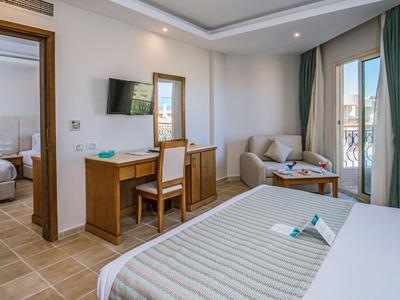 Habitación de hotel luminosa con cama doble, escritorio, sofá y balcón con vista al mar.