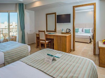 Habitación de hotel con dos camas individuales, escritorio y acceso a otra habitación con cama y balcón.