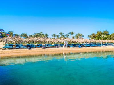 Pláž s lehátky a slunečníky u čisté modré vody pod modrou oblohou