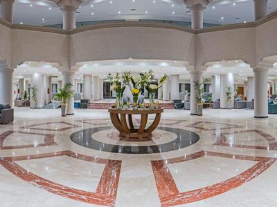 Gran vestíbulo de hotel elegante con suelo de mármol y decoración floral central bajo techo abovedado.