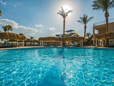 Piscina blu con luce solare, palme e sedie a sdraio sotto un cielo azzurro.