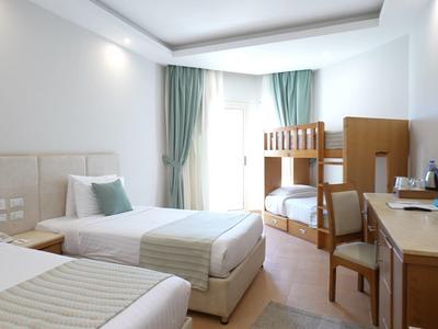 Habitación de hotel luminosa con dos camas individuales, litera, escritorio y cortinas en la ventana.