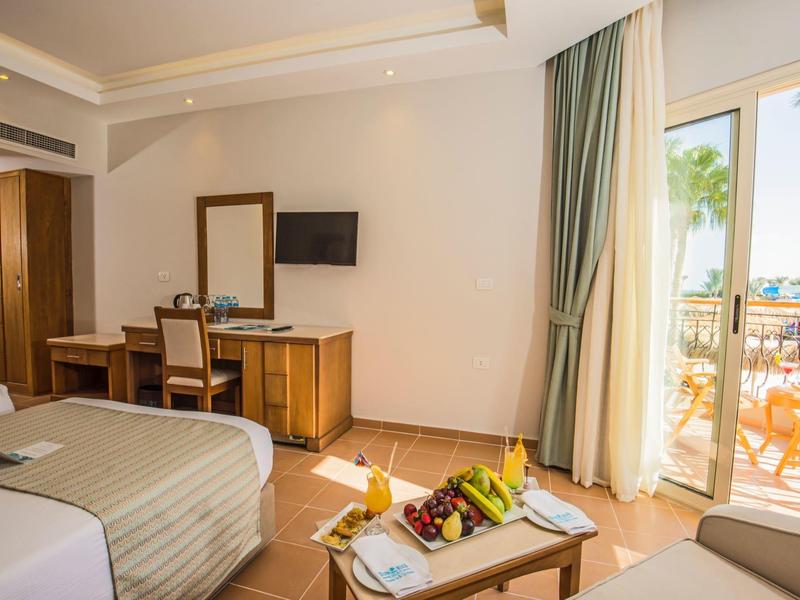 Habitación de hotel luminosa con camas, balcón y vista al mar bajo cielo despejado.