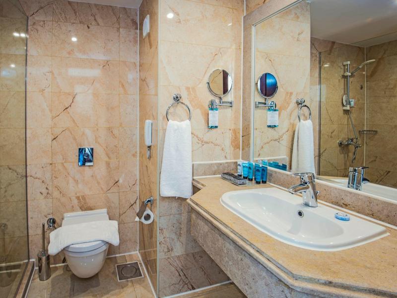 Baño de hotel con paredes de mármol, lavabo, inodoro y toallas.