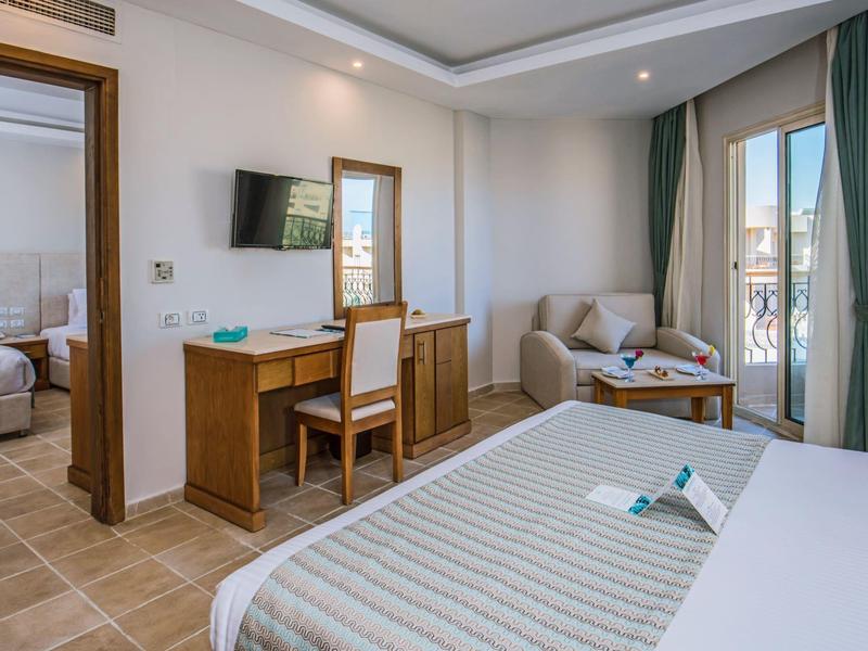 Habitación de hotel luminosa con cama doble, escritorio, sofá y balcón con vista al mar.