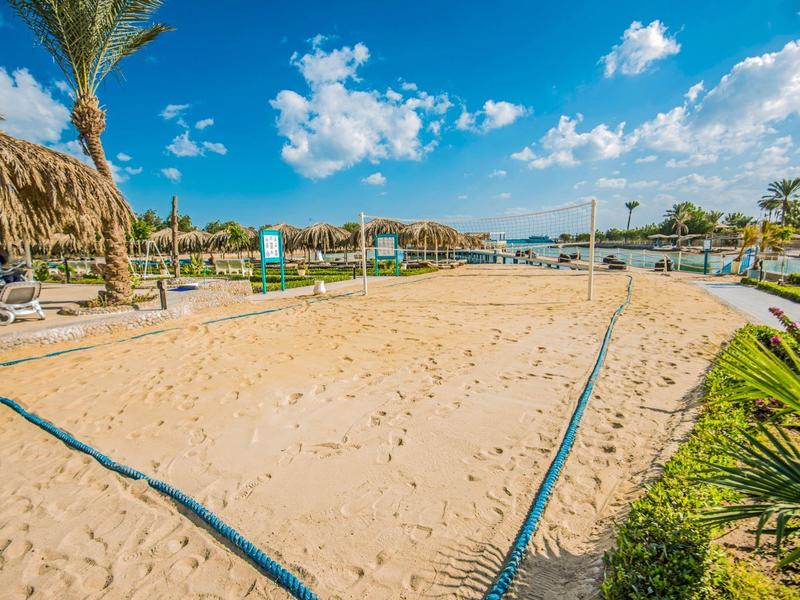 Cancha de voleibol de playa arenosa con líneas azules y palmeras en un resort soleado.