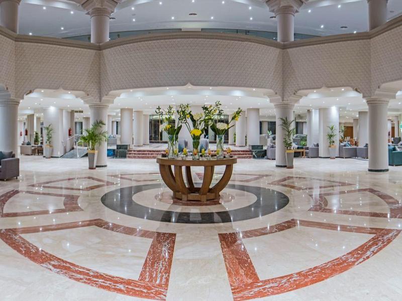 Gran vestíbulo de hotel elegante con suelo de mármol y decoración floral central bajo techo abovedado.