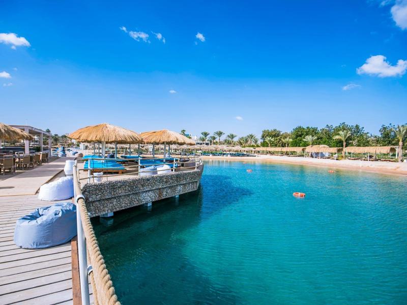 Agua turquesa clara en una playa soleada con muelle y techos de paja.