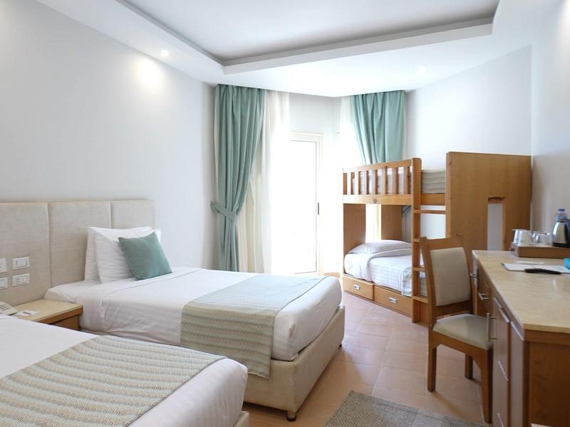 Habitación de hotel luminosa con dos camas individuales, litera, escritorio y cortinas en la ventana.