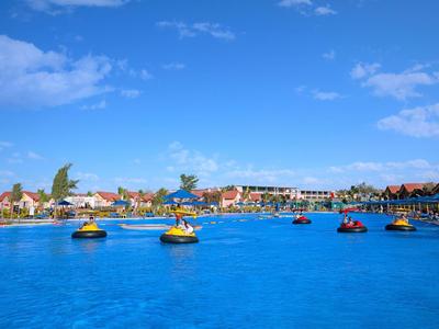 Groot blauw zwembad met waterfietsen en hotels op de achtergrond onder een blauwe lucht.