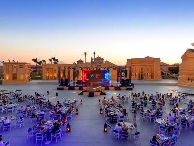 Groot openlucht evenement met podium en tafels bij zonsondergang.