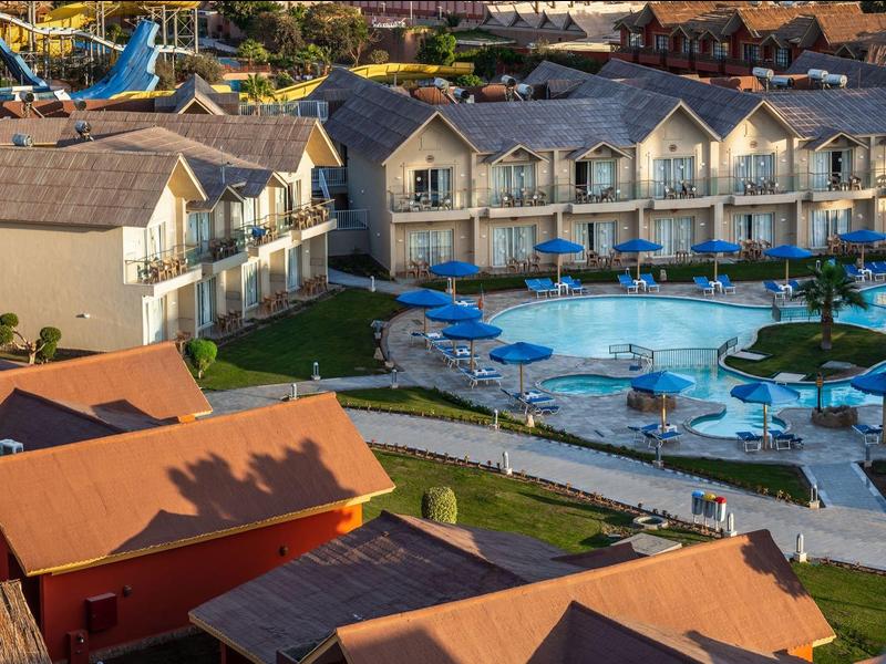 Ośrodek z dużym basenem otoczonym leżakami i przylegającymi dwupiętrowymi budynkami hotelowymi.