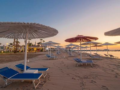Leere Liegestühle mit Sonnenschirmen am Sandstrand bei Sonnenuntergang.
