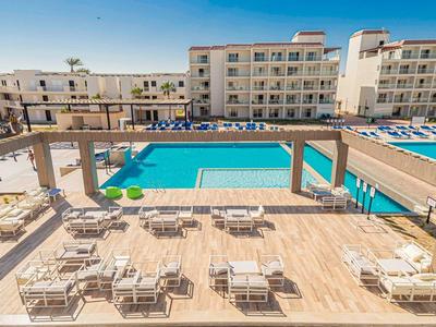 Terasa s lavičkami a židlemi vedle bazénu v hotelovém komplexu.