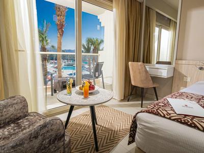 Helles Hotelzimmer mit Doppelbett, Sessel, Tisch mit Früchten und Balkon mit Meerblick.