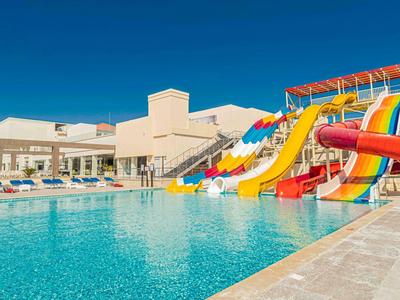 Großer Poolbereich mit Wasserrutschen und Liegestühlen unter blauem Himmel.