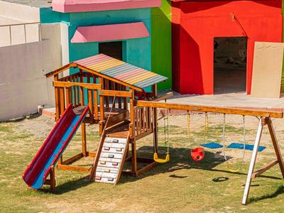 Bunter Kinderspielplatz mit Rutsche, Kletterwand, Schaukel und Holzhäuschen auf Grasfläche.