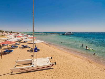 Sandstrand mit Liegestühlen, Sonnenschirmen und ruhigem Meer unter klarem Himmel.