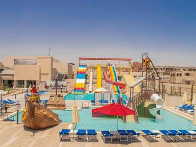 Wasserpark mit bunten Rutschen, blauen Liegen und Sandbecken unter klarem Himmel.