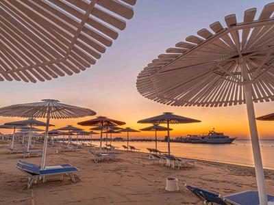 Sonnenuntergang über einem ruhigen Strand mit Liegestühlen und Sonnenschirmen