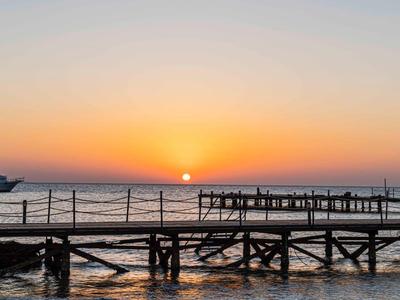 Sonnenuntergang am Meer mit Holzsteg und Boot im ruhigen Wasser, Himmel in warmen Farben.