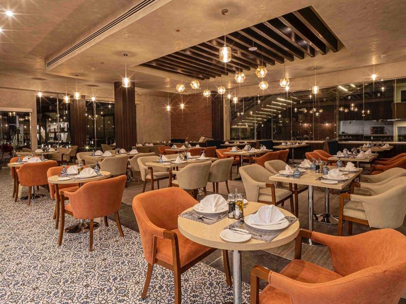 Modernes Restaurant mit warmem Licht, runden Tischen und orangefarbenen Sesseln, gemütliche Atmosphäre.