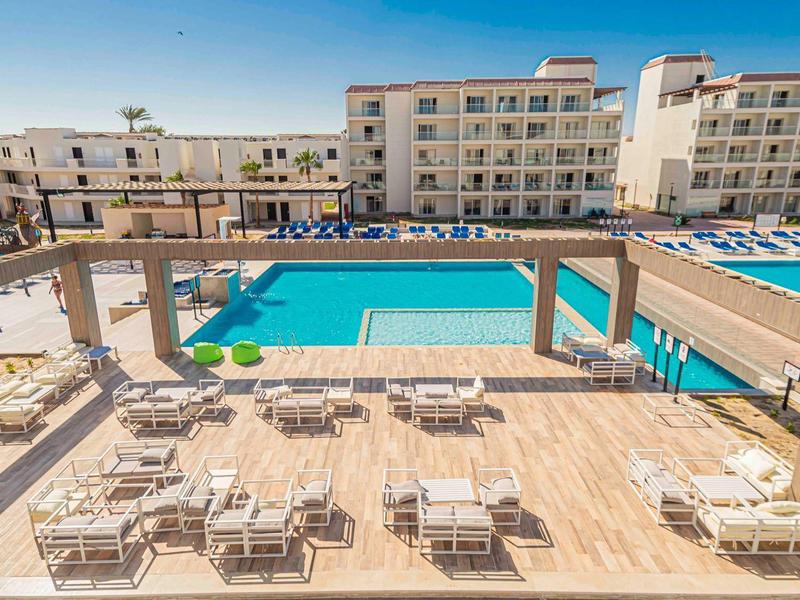 Balkon mit Stühlen und Tischen, Blick auf Pool und umliegende mehrstöckige Wohngebäude.