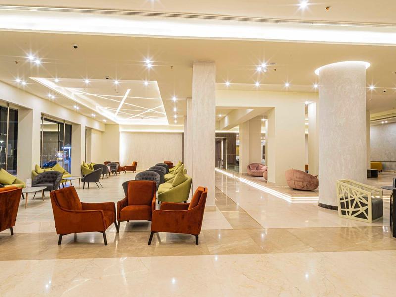 Heller Hotel-Lobby mit bequemen orangefarbenen Sesseln, Säulen und glänzendem Boden.