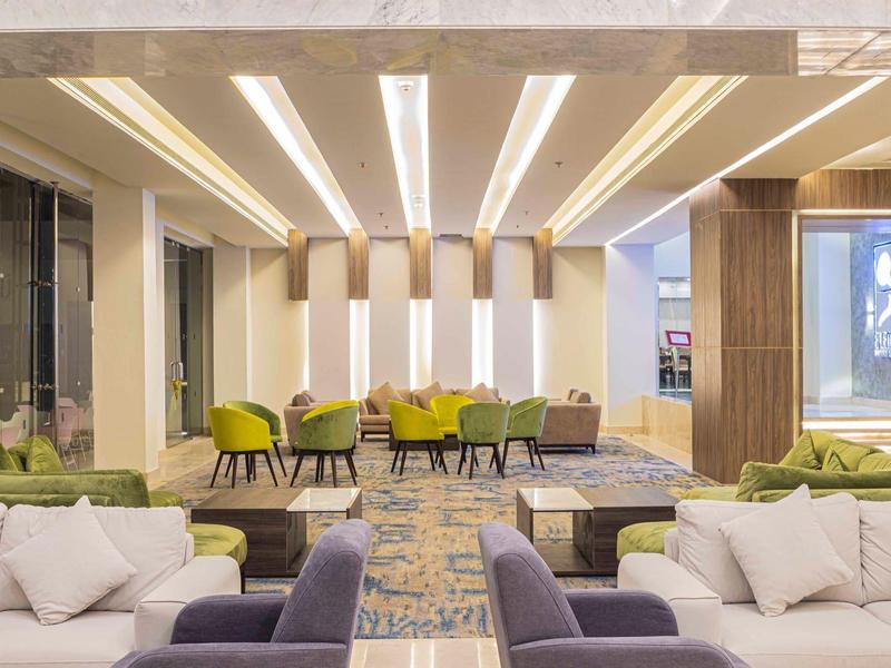 Heller, moderner Wohnraum mit weißen Sofas, grünen Stühlen und Holzelementen, großzügig und einladend gestaltet.