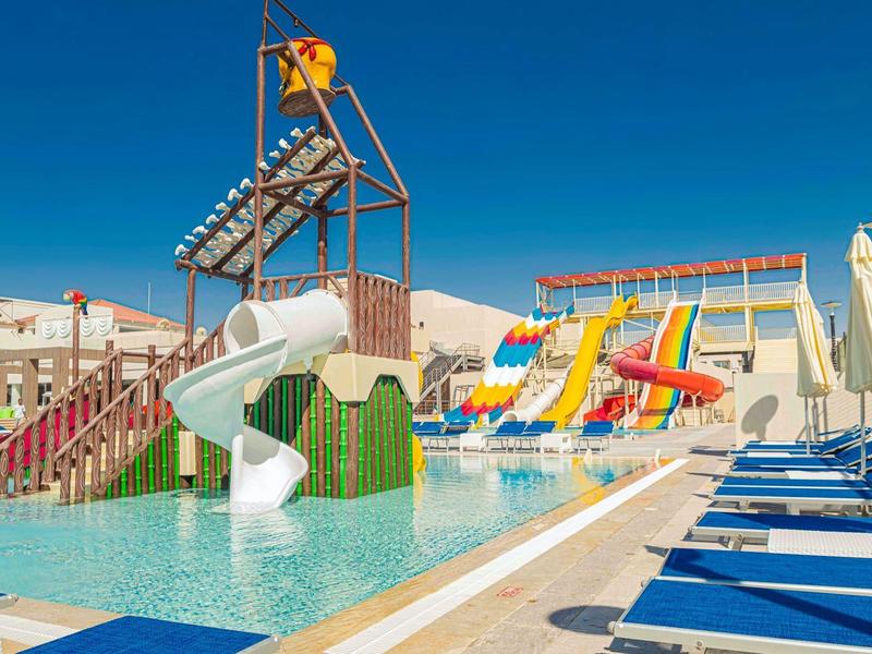 Wasserpark mit bunten Rutschen, Swimmingpool, blauen Liegestühlen und klarem Himmel.