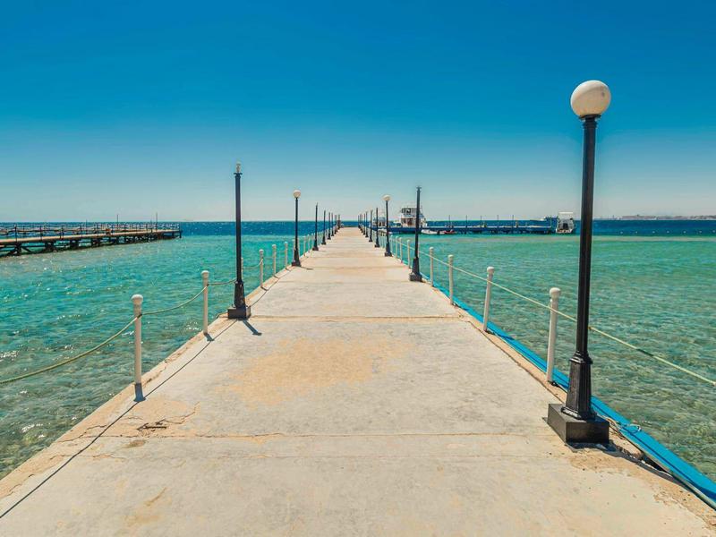 Langer Steg mit Lampen über türkisfarbenem Wasser unter klarem blauem Himmel.