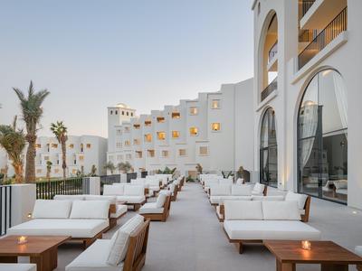 Moderne buitenruimte van een hotel met witte zitplaatsen en palmbomen bij schemer.