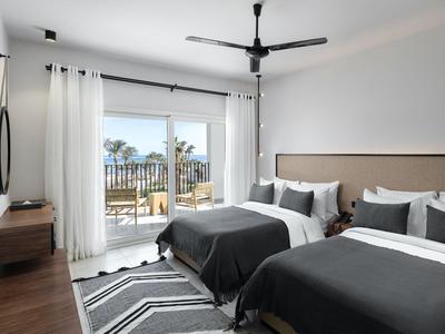 Moderne hotelkamer met twee bedden, balkon en uitzicht op palmbomen en water.