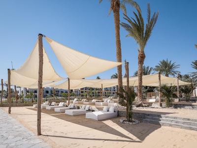 Vrijetijdsgebied met ligstoelen en schaduwzeilen bij een strandresort met palmbomen.