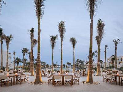 Buitenrestaurant met houten tafels en palmbomen in een warm Aziatisch strandresort.