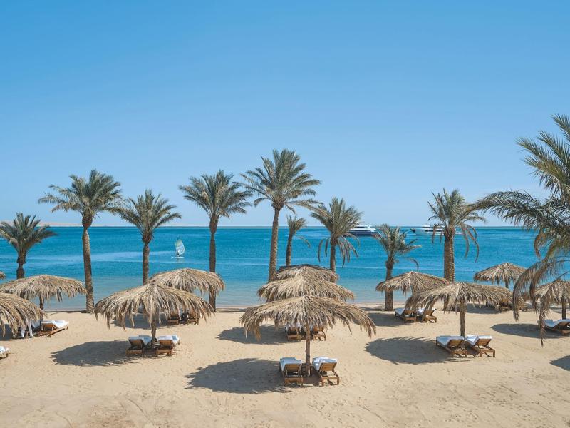 Strand mit Palmen und Strohdächern, blauer Himmel und Meer im Hintergrund.