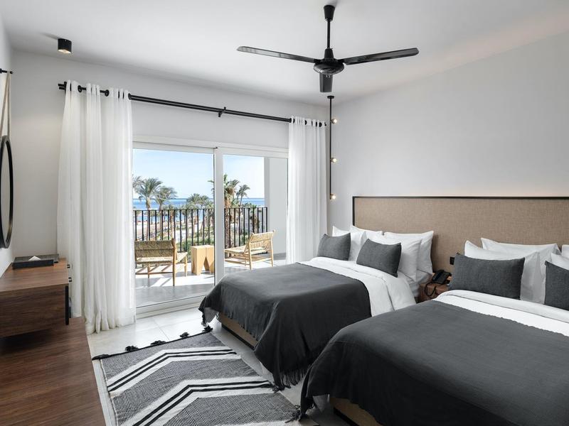 Modernes Hotelzimmer mit zwei Betten, Balkon und Blick auf Palmen.