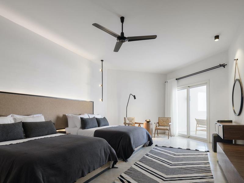 Modernes Zimmer mit zwei Doppelbetten, grauem Teppich, Schreibtisch und Balkon mit weißen Wänden.