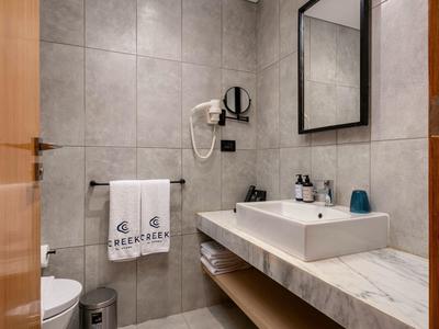 Modernes Badezimmer mit grauen Fliesen, weißen Waschbecken, Handtüchern und Haartrockner an der Wand.