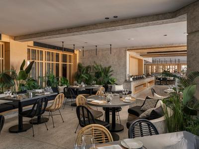 Espace lounge d'hôtel moderne avec tables, chaises et beaucoup de verdure dans un cadre lumineux.