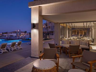 Vue extérieure en soirée d'une terrasse d'hôtel avec espace salon et piscine éclairée.