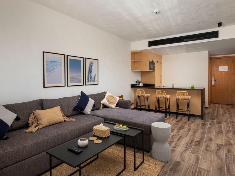 Modern eingerichtetes Wohnzimmer mit grauem Sofa, Couchtisch und Küchenbereich im Hintergrund.