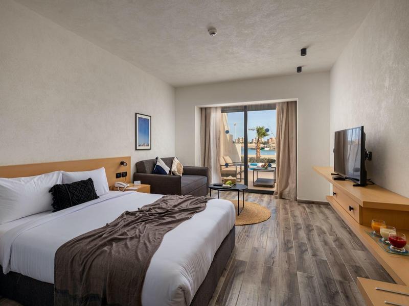 Modernes Hotelzimmer mit Doppelbett, Sofa und Balkon mit Meerblick.