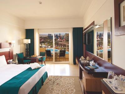 Bright hotel room with double bed, seating area, and balcony overlooking the sea.