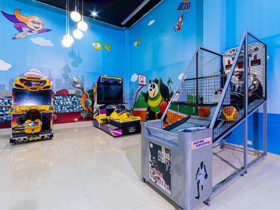 Kleurrijke speelruimte voor kinderen met arcadegames en basketbalring in een helderblauwe omgeving.