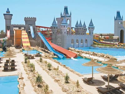 Water park with castle-themed slides and pools, surrounded by sunbeds and umbrellas.