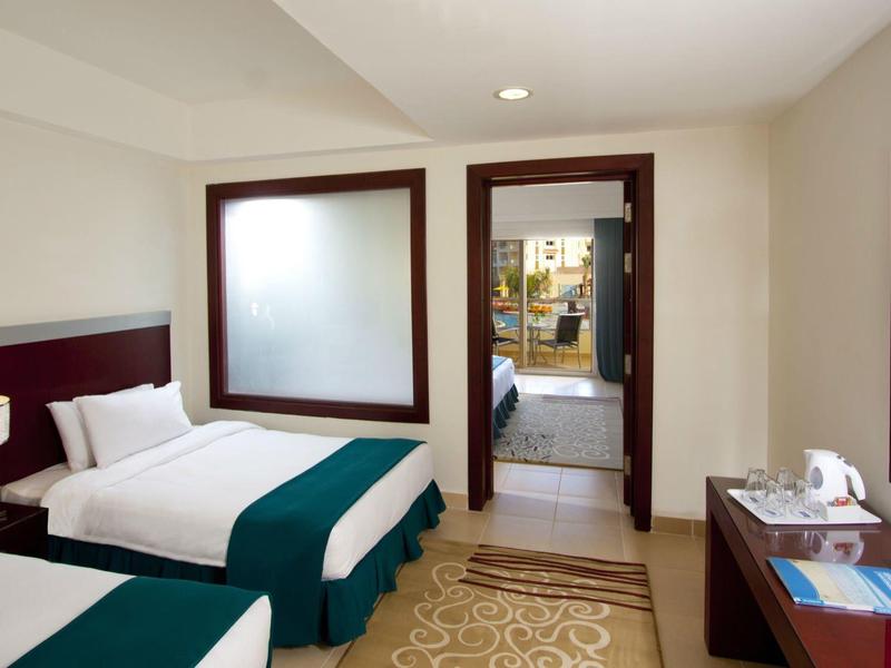 Hotel room with two single beds, nightstand, mirror, and desk with chair.