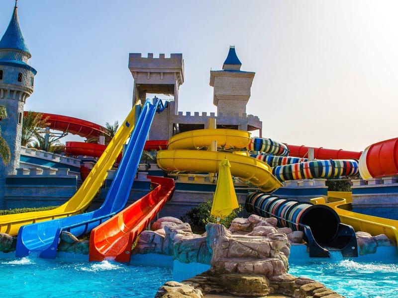 Colorful water slides lead into a pool in front of a castle-themed water park.